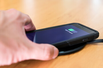 Men hand putting smartphone on wireless battery charge. New technology that allow to recharge mobile phone without wire charger or inductive charging.