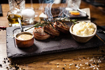 Pork tenderloin with mashed potatos, bacon and mustard sauce with branch of smoking rosemary. Delicious healthy traditional grilled meat food served for lunch in modern cuisine gourmet restaurant.
