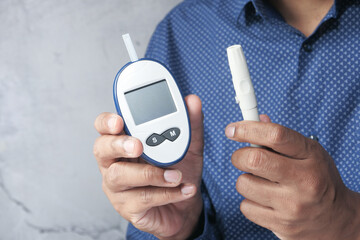 Man hand holding diabetic blood test kit glucometer on color background .