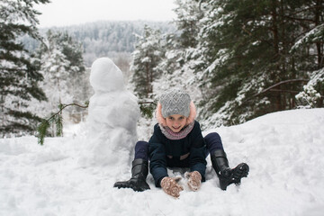 Cute little girl with snowman in winter snowy Park.