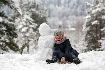 Fototapeta na wymiar Cute little girl posing with snowman in winter snowy Park.