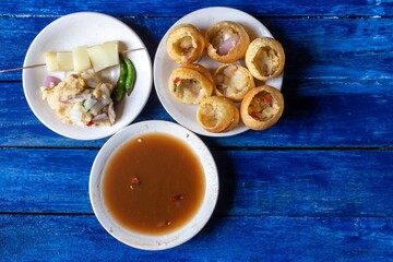 Panipuri or Golgappa with Tamarind Chutney, Chili and Spicy Potato Stuff in Plates Isolated on Blue Wooden Background in Horizontal Orientation, Also Known as Phuchka, Paani Patashi, Gup Chup