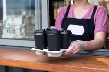 Fototapeta na wymiar Barista in an apron holds hot coffee in a paper cup in his hands. Coffee pick up at cafe shop.