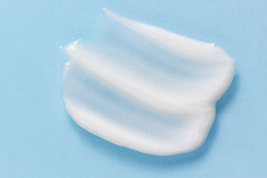 Face wash texture. White pore cleansing foam gel smear smudge on pastel blue background. Skincare exfoliating powder cream closeup