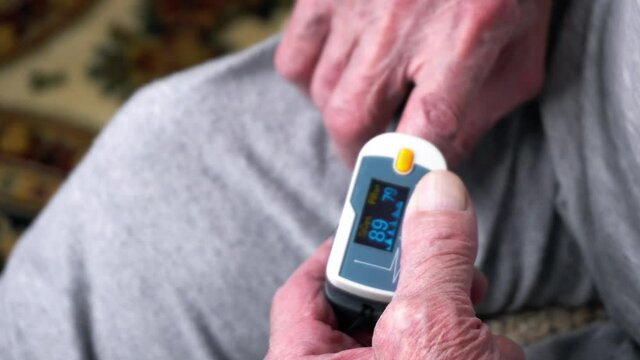 Old man is using pulse oximeter at his finger to measure his pulse. The aged man is putting the device on and checks the level of vital statistics. Theme of using medical equipment in treatment.