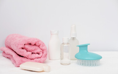 Fototapeta na wymiar travel set for hair care. modern hair massage brush, shampoo, lotion and hair oil. pink towel on white background. essential toiletries for travel.