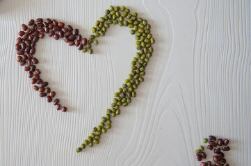 Adzuki beans and mung beans arranged as heart-shaped on white desk, copy space