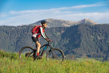 pretty senior woman riding her electric mountain bike on the mountains above Oberstaufen, Allgau Alps, Bavaria Germany 
