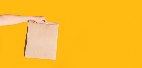 Millennial woman holding paper bag with takeaway food on orange background, empty space