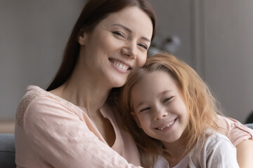Close up portrait of smiling young Caucasian mother and small daughter hugging and cuddling at...
