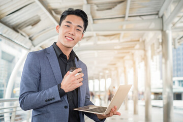 Portrait of Asian businessman holding laptop and coffee cup in the building office city