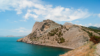 View of the blue Black Sea, and a high cliff against a blue cloudy sky.