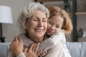 Cute caring small granddaughter embrace cuddle smiling middle-aged 60s grandmother, relax together...