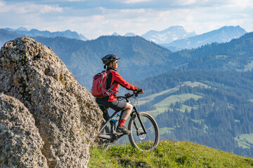 Obraz premium pretty senior woman riding her electric mountain bike in warm dawn sunlight and enjoying the spectacular view over the Allgau alps near Oberstdorf, Bavaria, Germany