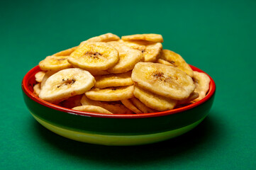 Healthy snack, crispy dehydrated unsugared banana chips in bowl on green background