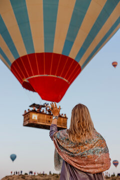 Beautiful blonde woman greets flying hot air balloon at dawn in Cappadocia