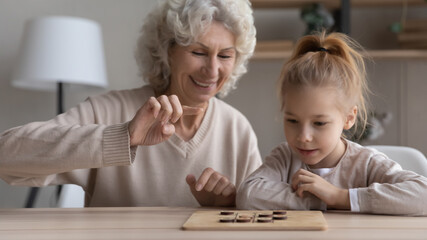 Happy middle-aged mature grandmother and small granddaughter have fun play wooden game at home...