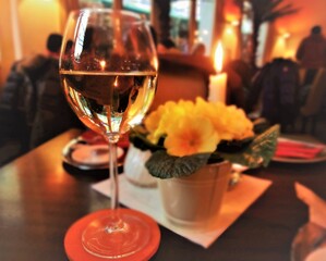 A glass of white wine and a festively decorated table in a small cafe on New Year's Eve. In the background a candle burns.