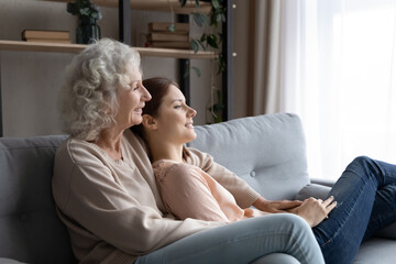 Happy elderly mother and grownup daughter relax on comfy sofa in living room look in distance dreaming visualizing, smiling dreamy mature mom and adult girl child rest on couch, enjoy leisure weekend