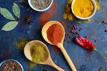 Closeup wooden spoons with green and orange spices, cups with dried herbs on a dark background. Top view. Fragrant cuisine concept