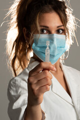 Close up of woman wearing medical uniform showing a phial on a grey background. Focus on phial