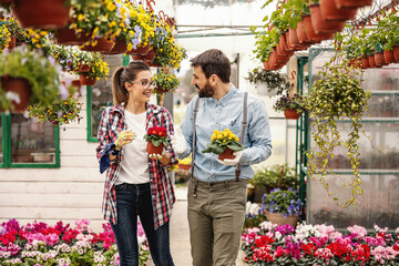 Fototapeta premium Gardeners walking in greenhouse and talking and carrying pots with flowers.