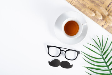 Happy Father Day background concept with newspaper, leaf, black mustache, glasses and cup of tea on white background with copy space for text.