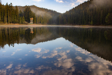 Foggy surface and forest reflection of Synevyr lake in the early morning. The biggest mountain lake in Ukraine on beautiful spring morning.