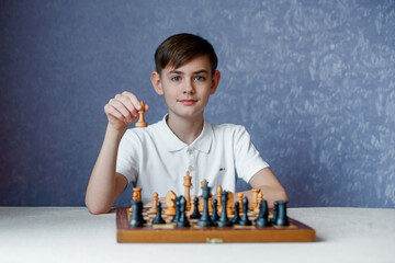 A cute boy in a white sweater next to a chess board, plays a game with himself and smiles. © svetlana1983