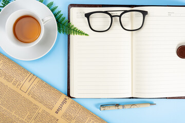 Happy Father Day background concept with notebook, pen, leaf, cup of tea, glasses and newspaper on blue background with copy space for text.