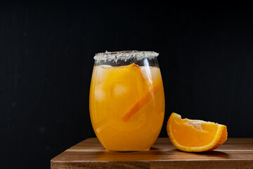 A glass of cold orange juice with ice cubes standing on wooden table together with orange slice