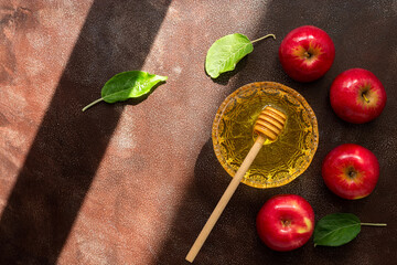 Red apples and honey on a dark background with shadows and sunlight. Top view, flat lay, copy space.
