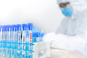 Medical scientist in personal protective equipment suit (PPE), mask and gloves doing research of COVID-19 in hospital laboratory. Doctor getting result of Coronavirus case. Focus on test tube on rack.