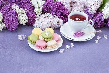 Fototapeta na wymiar on a lilac background a cup of tea, macaroons and a bouquet of lilacs