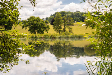 The lake at Fonthill Estate in Wiltshire, South West England.  The photo is framed with foliage on both sides and shows nature reflected in the water.