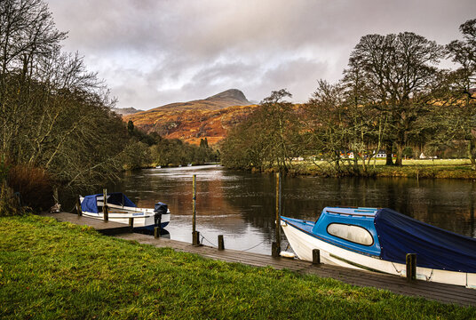 Two boats moored at the private jetty on River Dochart in Killin, with one of the peaks of the Tarmachan ridge in the background.