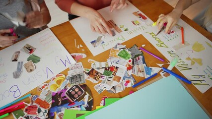 Group of four unrecognizable women sitting at table and making vision board collages to visualize their goals, dreams and plans for future during female training workshop, from above panning shot