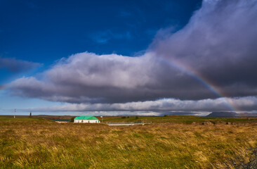 Rainbow, volcanic landscapes and farms in southern Iceland