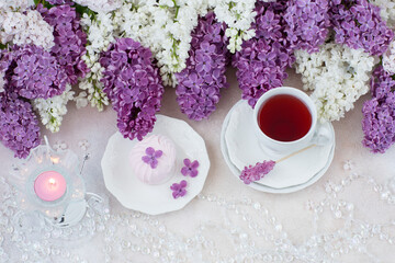 on the table are tea and marshmallows, beads, a candle in a candlestick and a bouquet of lilacs 