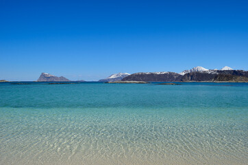 majestic white springtime beach with snowy mountain islands in sea on the summer island in northern norway