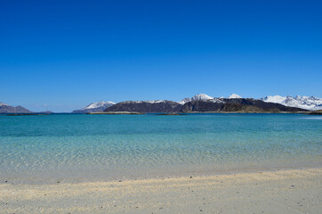 majestic white springtime beach with snowy mountain islands in sea on the summer island in northern norway