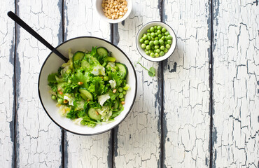 Mix salad leaves, cucumbers. pine nuts and green peas salad in white bowl