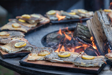 Fresh fish on the grill. A lemon wheel is placed on the fish. Fire can be seen in the middle.