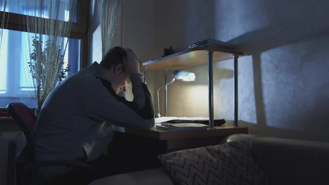 Student businessman working in a dark room with a desk lamp with documents. The student solves homework in his room in the evening.