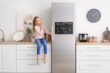 Little girl near chalkboard on refrigerator in kitchen