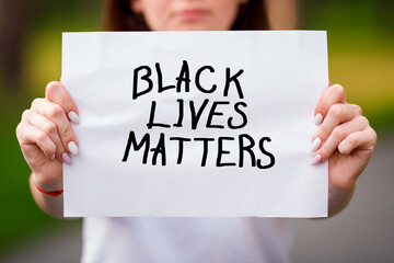 Blurred girl in outdoor holding a piece of paper with the words BLACK LIVES MATTERS in front of her.