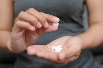 Close up of woman taking in pill she is pours the pills out of the bottle,taking painkiller to...