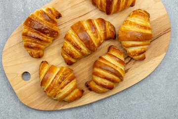 Wooden board with freshly baked croissants on gray background