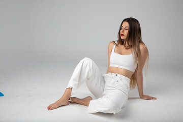 Fototapeta premium Modelo joven sentada sobre fondo blanco y ropa blanca con pelo largo