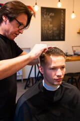 Fototapeta premium Barber is hairdressing the hair of young man with comb